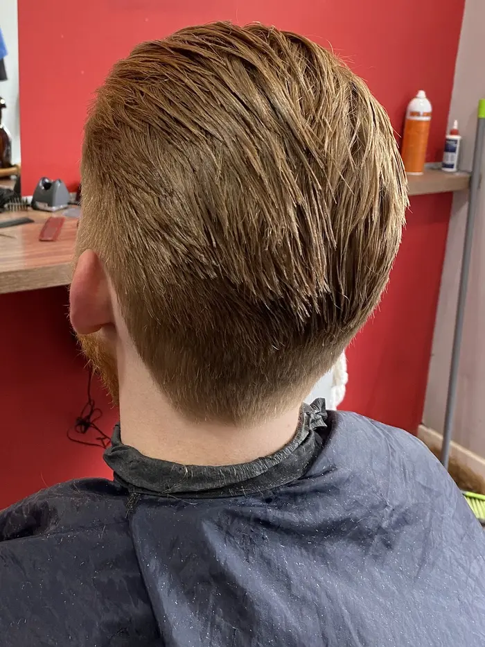 Neat tapered haircut against a red barbershop wall, back view